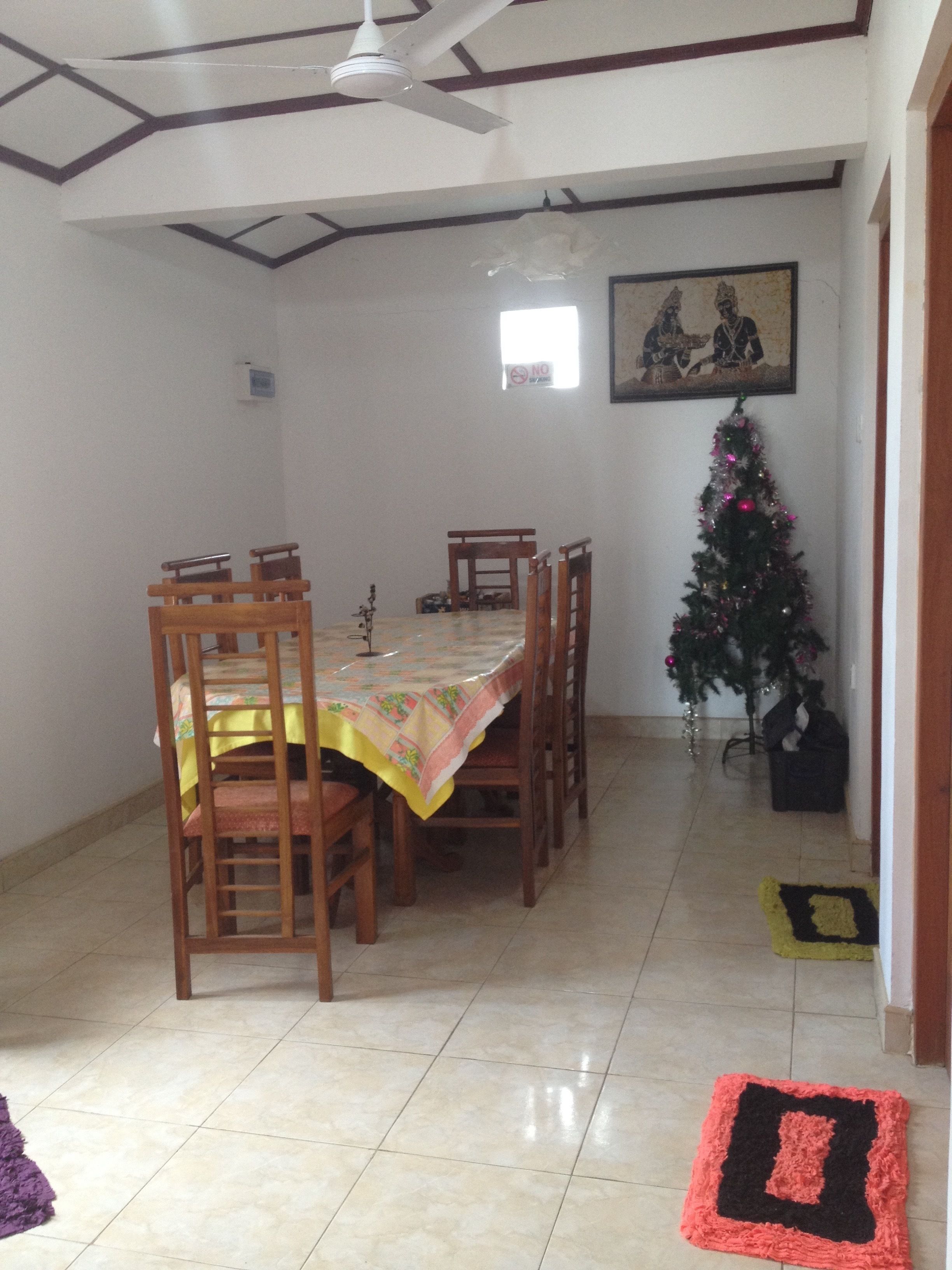 A dining area with a table set for four, a ceiling fan, a small Christmas tree, and a framed picture on the wall.