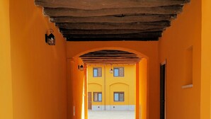 A corridor with yellow walls and a tiled floor, leading to a courtyard with a door and windows. - Corte Certosina (Trezzano sul Naviglio)