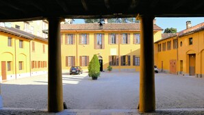 A courtyard with yellow buildings, a paved walkway, and a potted plant. - Corte Certosina (Trezzano sul Naviglio)