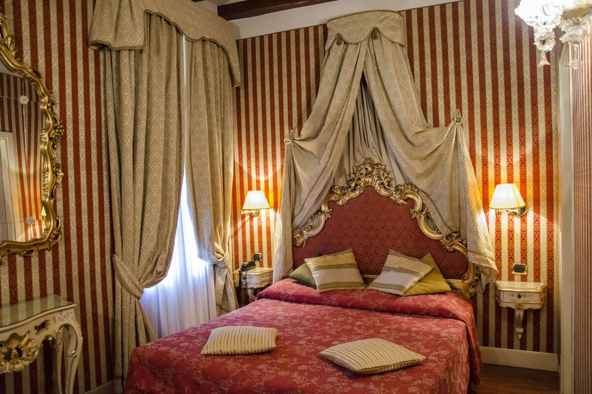 Una habitación con cama, cortinas, un espejo y dos lámparas de noche.