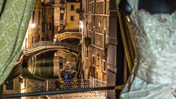 Une vue d’un pont historique et d’immeubles la nuit, avec un mannequin portant une robe au premier plan.