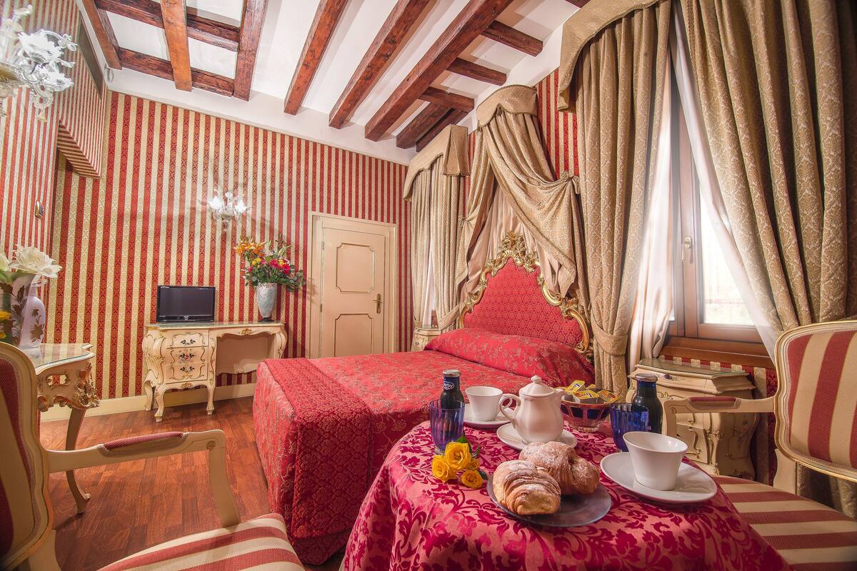 Una habitación con una cama, una mesa con provisiones para el desayuno, un televisor y un ventanal con cortinas.