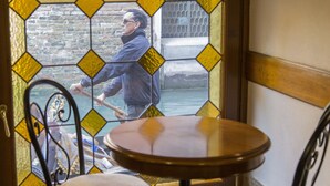 Une pièce avec une table et des chaises, une fenêtre donnant sur une personne qui rame dans un bateau, et un mur en briques.