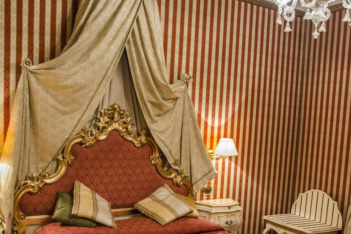 Una habitación con una cama con dosel, una araña y papel tapiz a rayas.