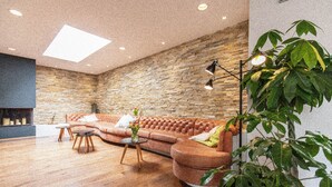 A modern living room with a stone wall, a leather sofa, a coffee table, and a floor lamp. - Hyve Hostel Basel (Basel)