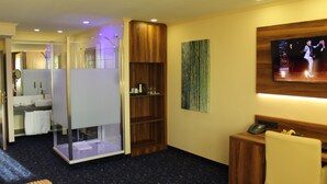A hotel room with a bathroom, a wooden cabinet, a TV, and a desk with a phone and bananas. - Grand Hotel Empire Frankfurt (Frankfurt)