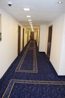 A long, narrow hotel corridor with a patterned carpet and recessed lighting.