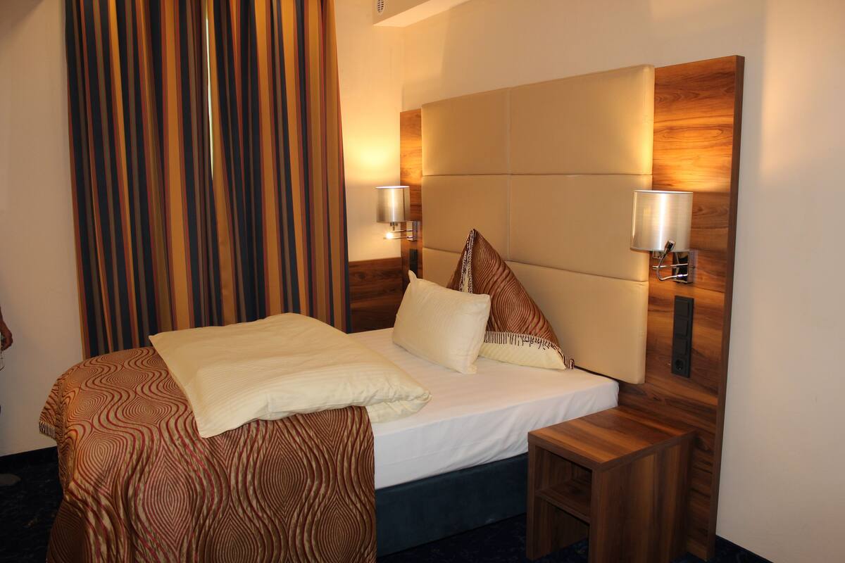 Quarto de hotel com uma cama grande, duas mesas de cabeceira, uma cabeceira de madeira e cortina listrada.