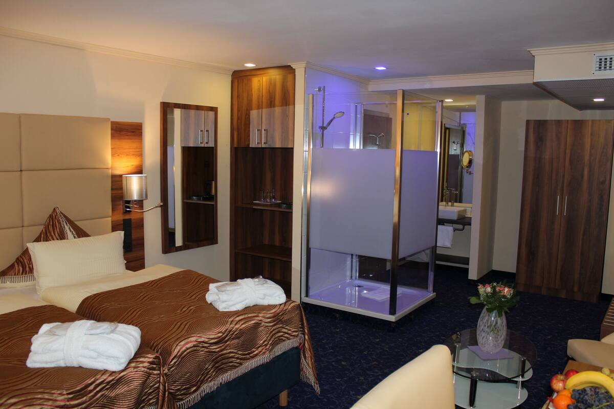 Quarto de hotel com cama, chuveiro, área de estar e uma pequena mesa com um vaso de flores.
