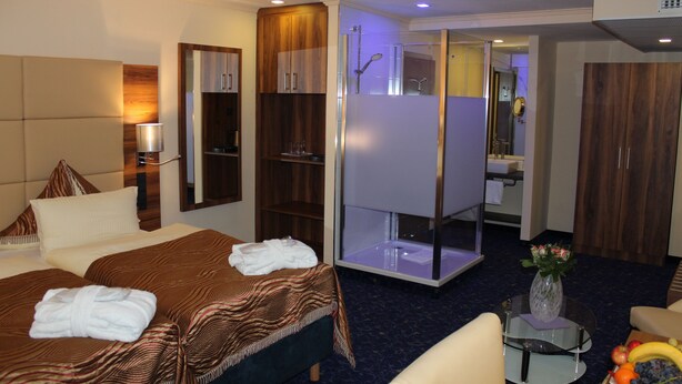 A hotel room with a large bed, a sitting area with a glass table, a shower area, and a wardrobe. - Grand Hotel Empire Frankfurt (Frankfurt)