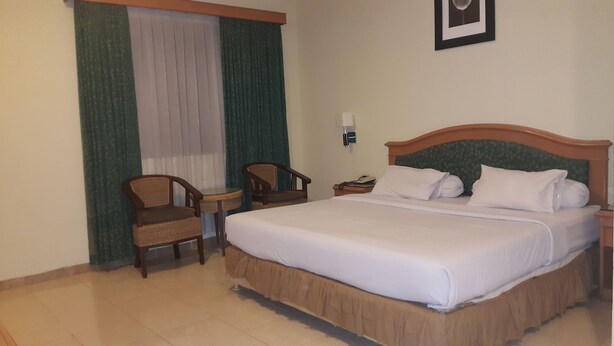 A hotel room with a large bed, two chairs, a small table, and a window with curtains. - Hotel Panakkukang (Makassar)