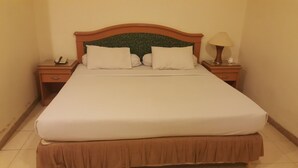A neatly made bed with a wooden headboard, two bedside tables with lamps, and a telephone on one of the tables. - Hotel Panakkukang (Makassar)