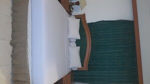 A hotel room with a bed, a wooden headboard, a green patterned curtain, and a nightstand with a lamp and a phone. - Hotel Panakkukang (Makassar)
