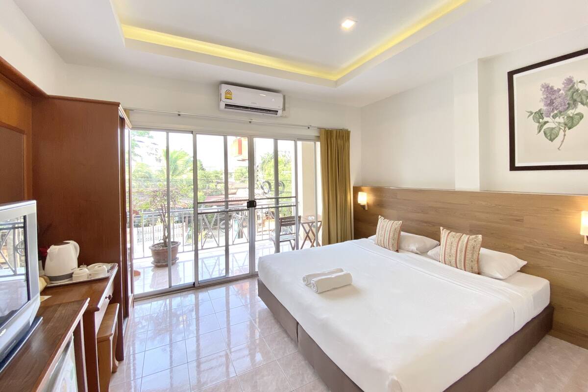 A hotel room with a large bed, a TV, a balcony with a view, and an air conditioning unit.