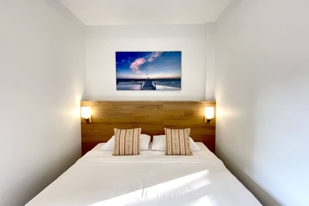 A neatly made bed with two pillows, a wooden headboard, and two wall-mounted lights.