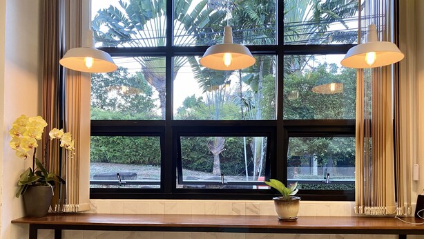 A bar area with a large window, a potted plant, and three stools. - Pensiri House (Sa Khu)