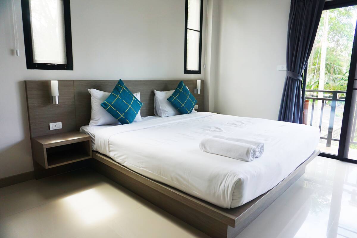A modern hotel room with a large bed, two pillows, a bedside table, and a window with curtains.