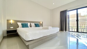 A modern hotel room with a large bed, a nightstand, a wall-mounted light, and a view of the outside through large windows. - Pensiri House (Sa Khu)