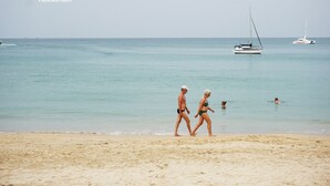 A beach scene with two people walking, a sailboat, and a swimmer in the water. - Pensiri House (Sa Khu)