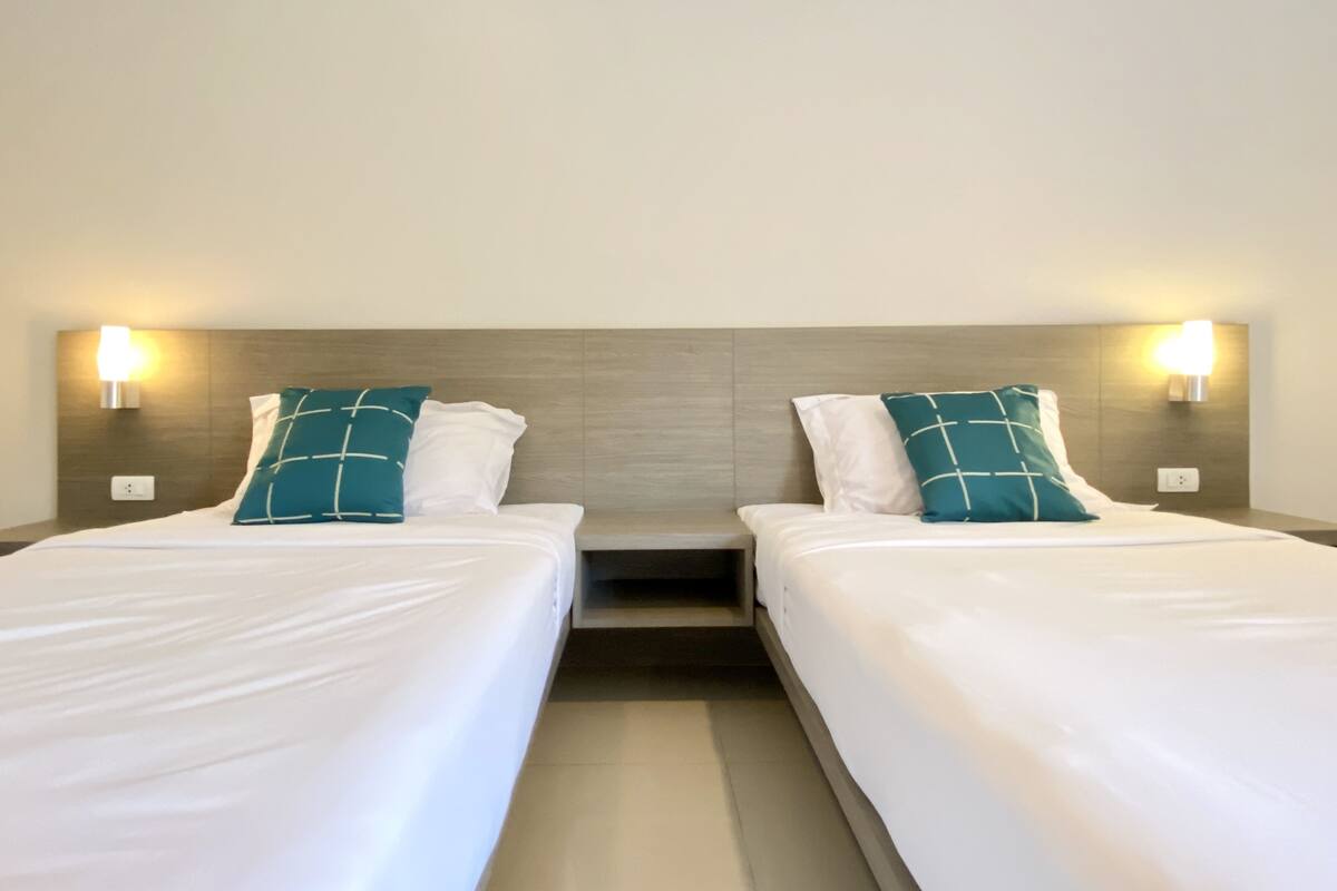 Two single beds with white linens and teal pillows, each with a wall-mounted light.