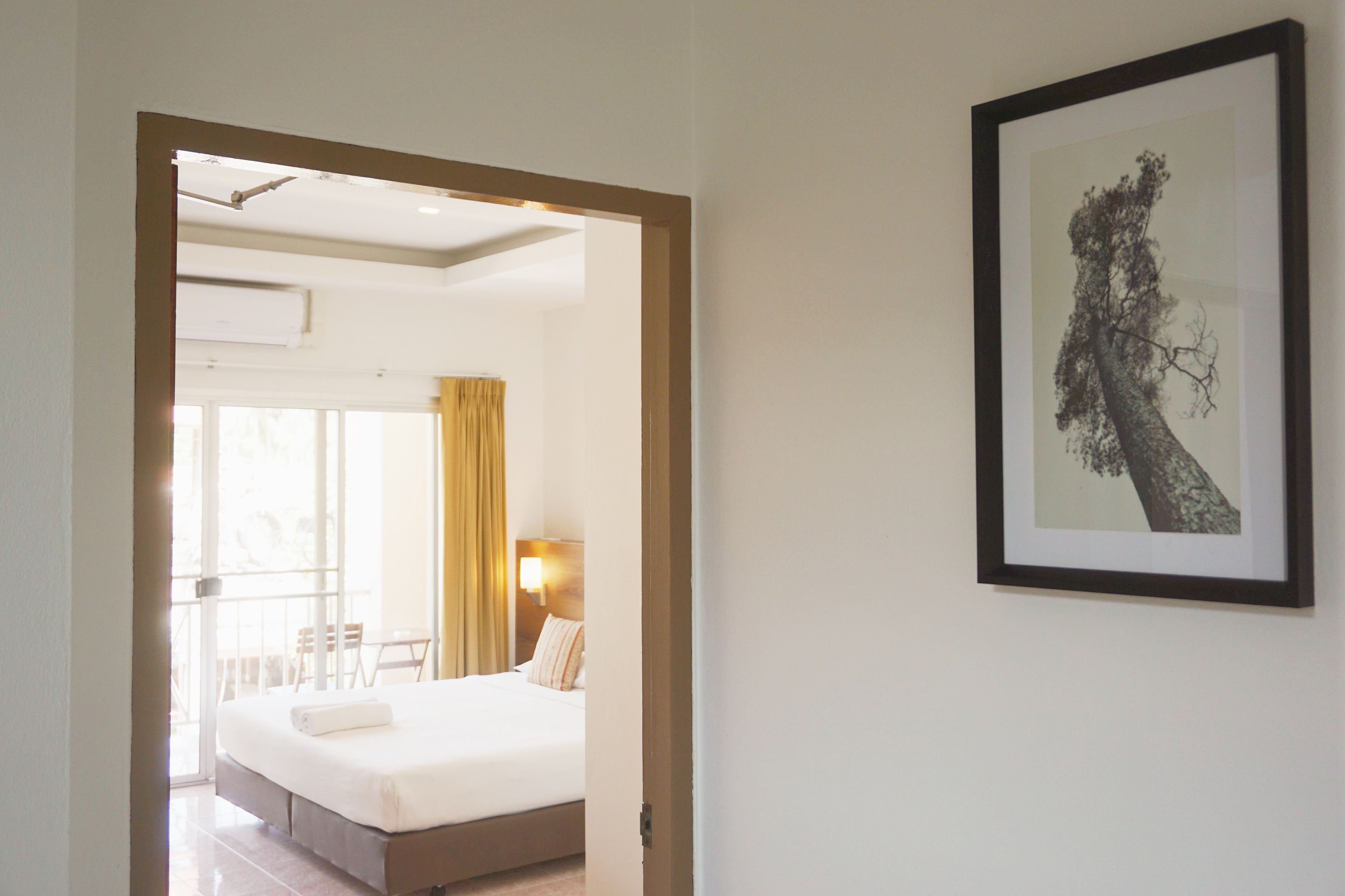 A hotel room with a large bed, a window with curtains, a framed picture on the wall, and a balcony with chairs.