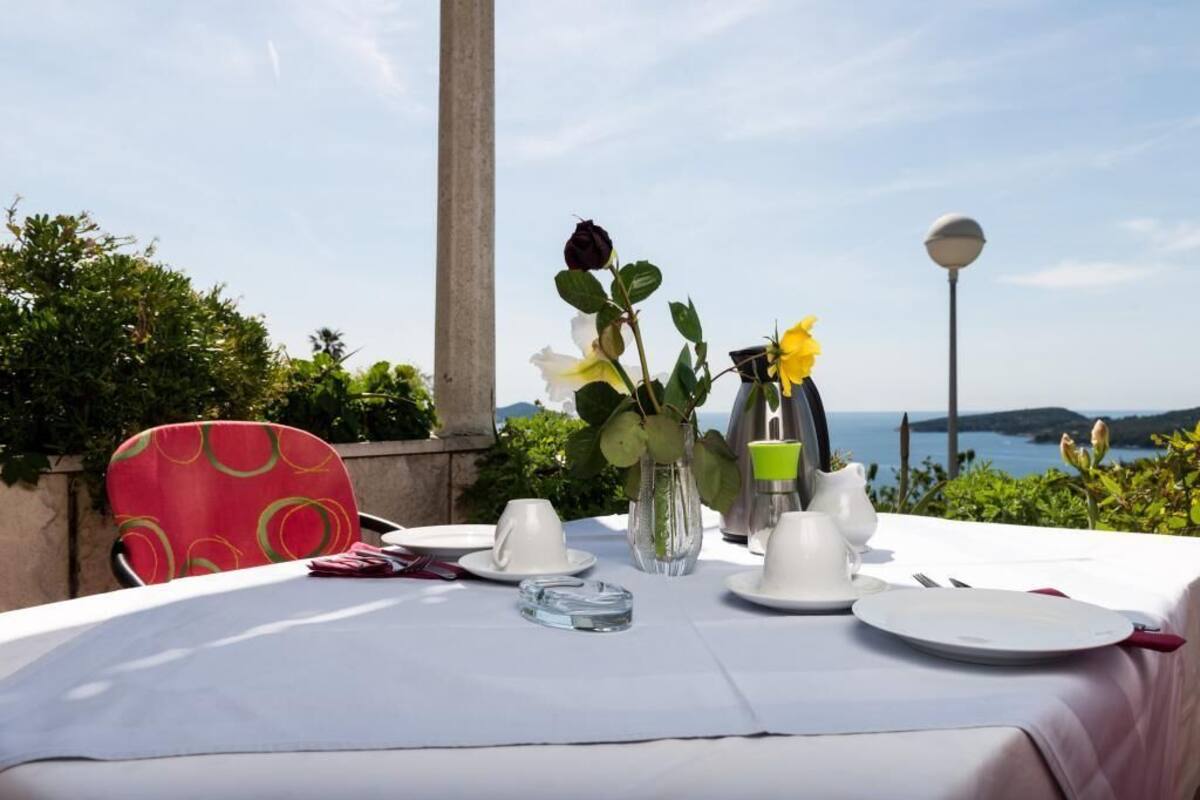A table set for two with white tablecloths, a vase with flowers, and a view of the sea.