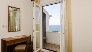 A room with a wooden desk, chair, and a large mirror. There is a sliding glass door leading to a balcony with a view of the sea. - Guesthouse Moretić (Dubrovnik)