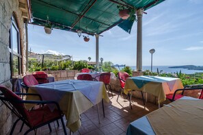 An outdoor dining area with tables and chairs, a view of the sea, and a mountainous backdrop. - Guesthouse Moretić (Dubrovnik)