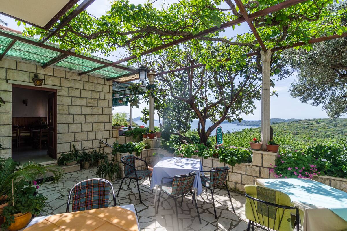 An outdoor patio with stone flooring, a table with a tablecloth, and chairs.