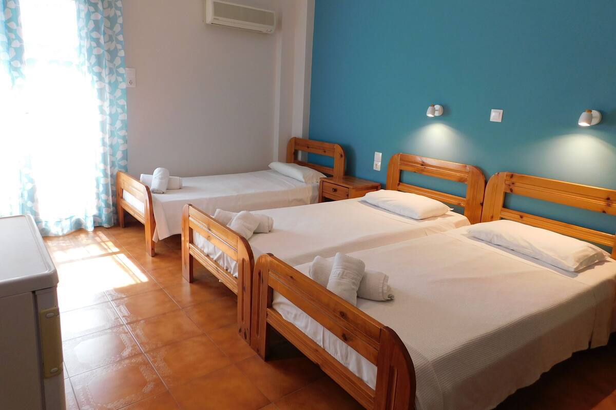 Een hotelkamer met twee houten bedden, een blauwe accentmuur en een raam met gordijnen.
