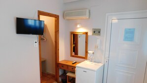 Une petite pièce avec une télévision, un miroir, une porte blanche et un petit réfrigérateur blanc.