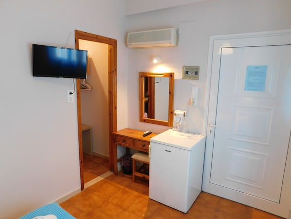 Une petite pièce avec une télévision, un miroir, une porte blanche et un petit réfrigérateur blanc.