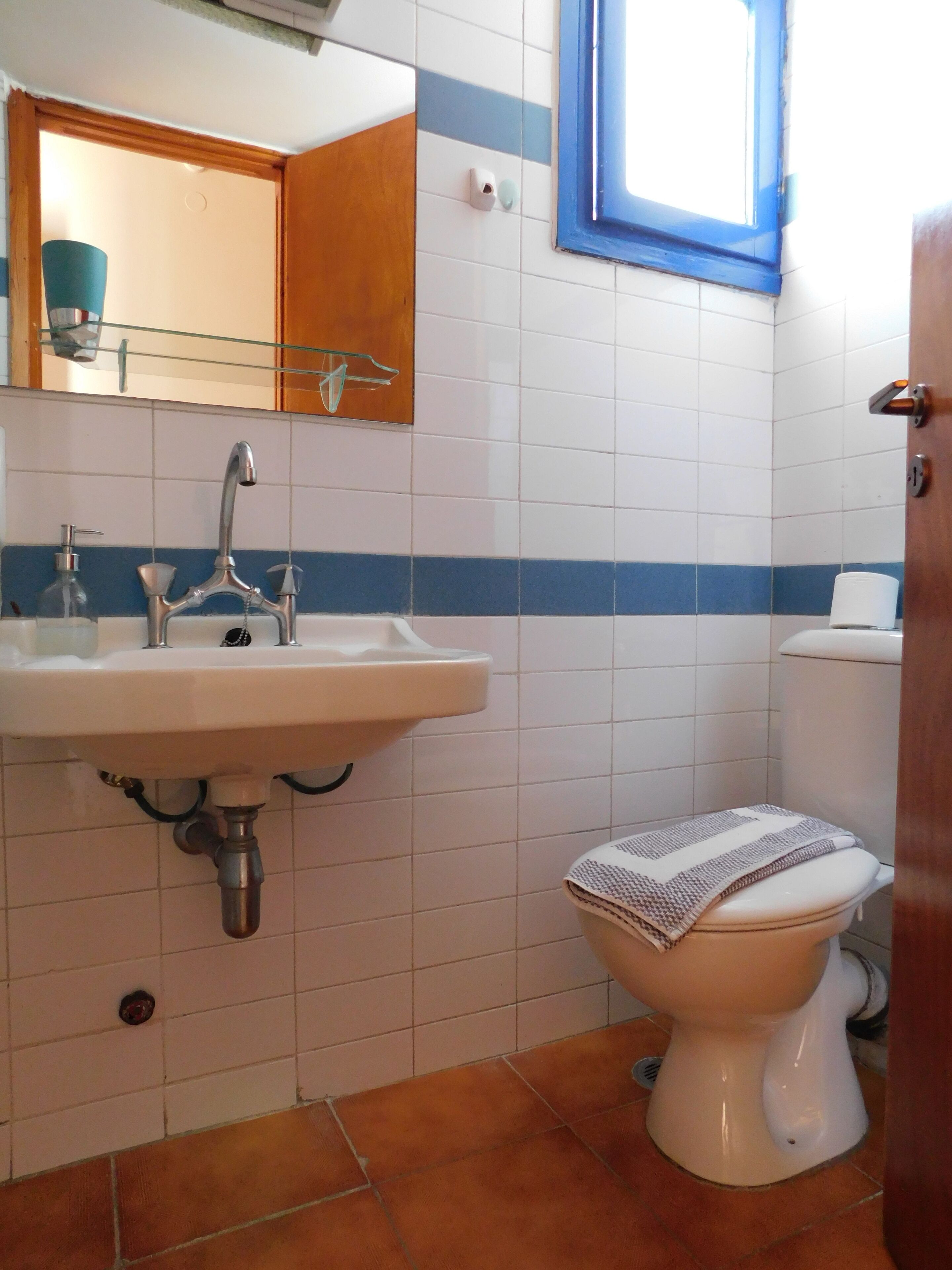 Un bagno con un lavandino bianco, uno specchio, una parete a righe blu, un water e una finestra.