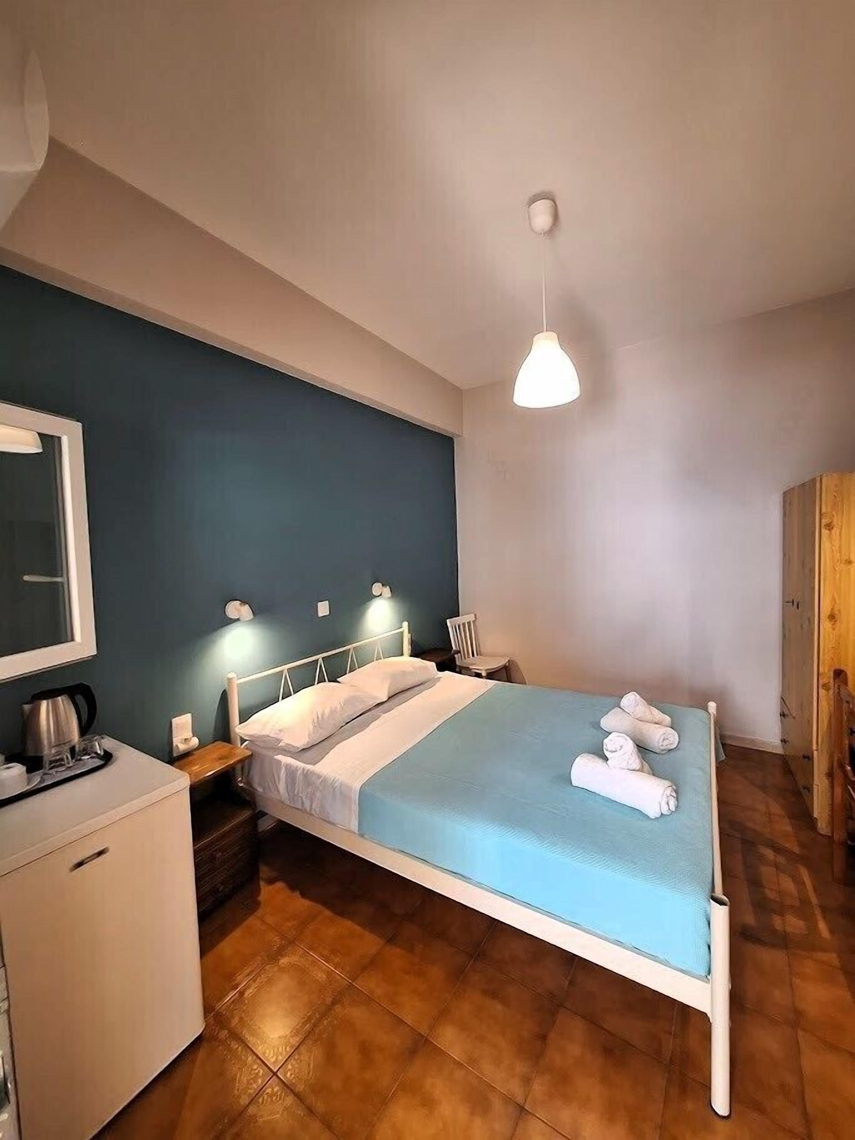 Un dormitorio ordenado con una cama, una mesita de noche y un pequeño escritorio con un hervidor y tazas.
