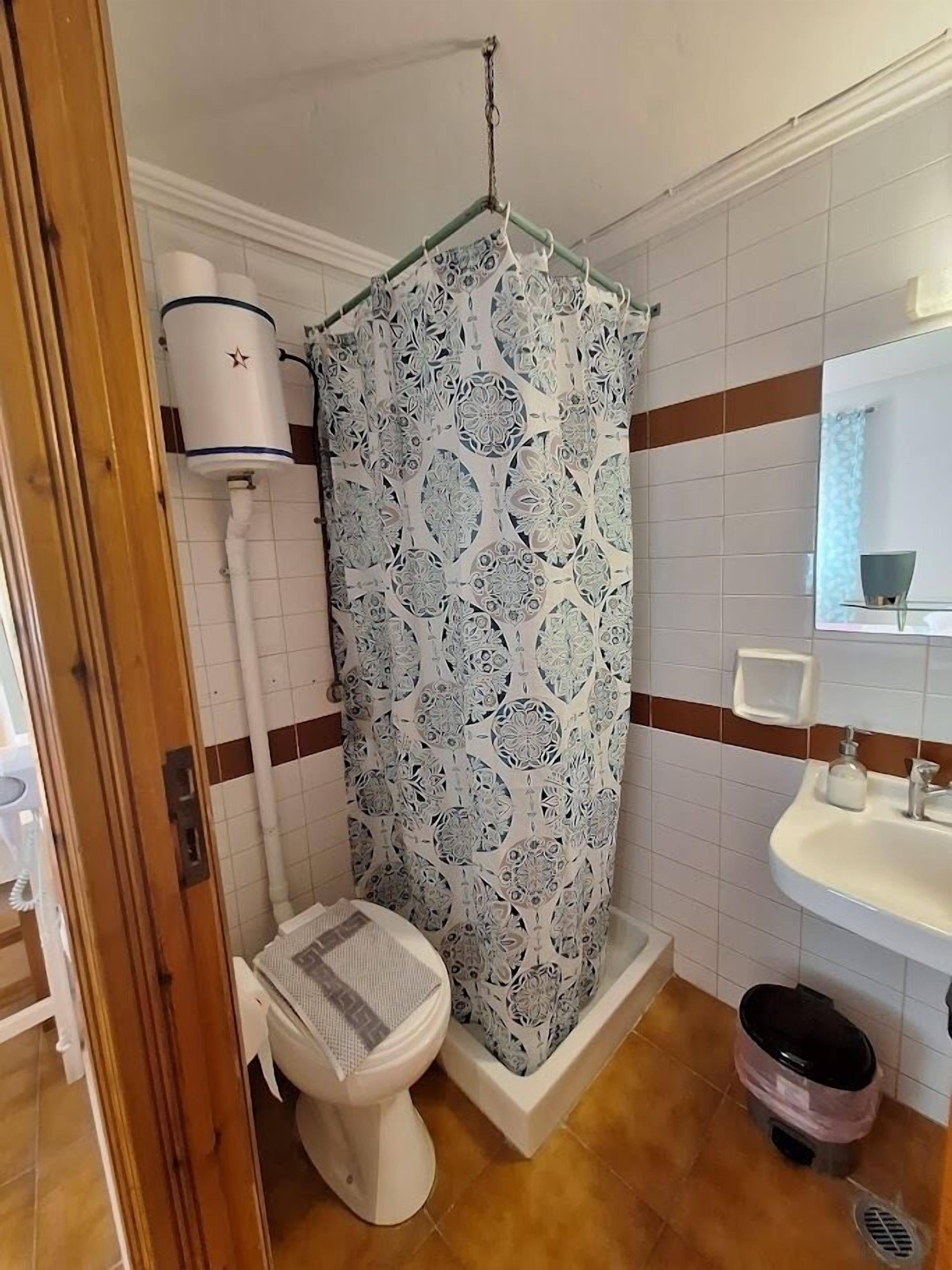 A bathroom with a toilet, shower curtain, sink, and a trash bin.