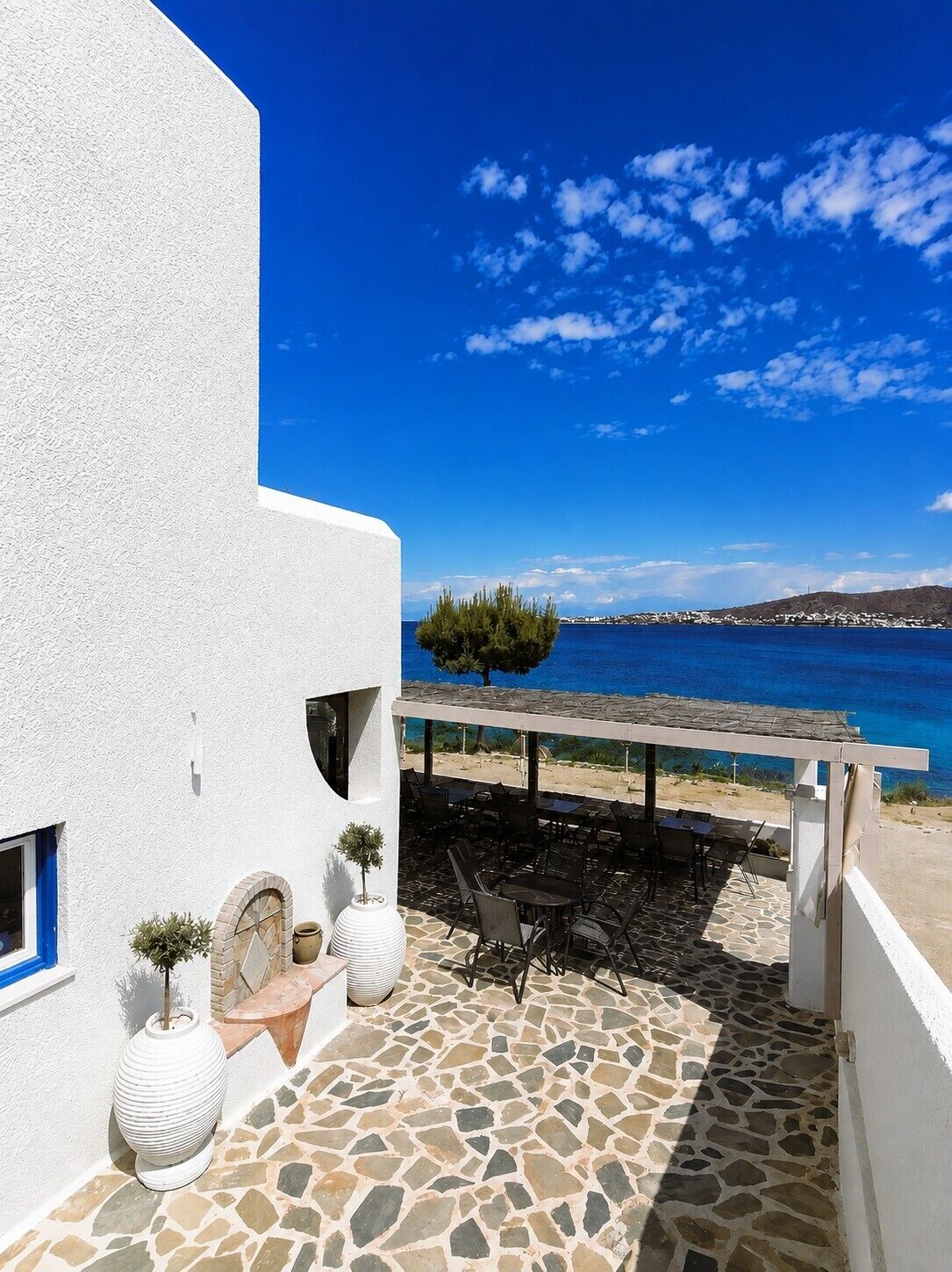 A coastal building with a stone patio, outdoor seating, and a view of the sea.