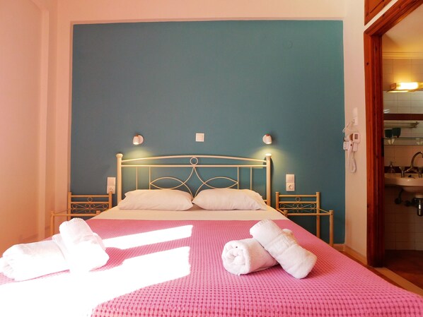 A bed with white linens, a pink textured bedspread, and rolled towels on the bed.