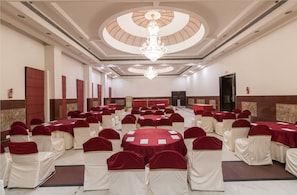 A banquet hall with round tables, white and red chairs, and a chandelier. - Hotel Pacific Dehradun (Dehradun)