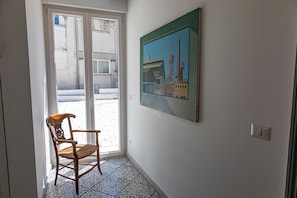A room with a door leading outside, a chair, a painting on the wall, and a light switch.