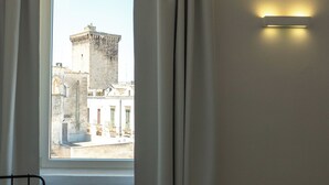 Ein Fenster mit Vorhängen, Blick auf ein Gebäude mit einem Turm und einer Wandleuchte.