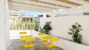 Eine Terrasses mit gelben Stühlen und Tischen, umgeben von Kakteen und kleinen Pflanzen.