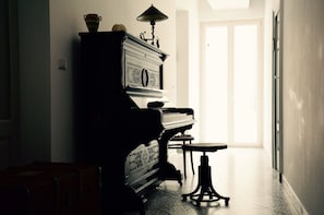 A piano, a table, and a lamp in a room with a door leading to a bright area.