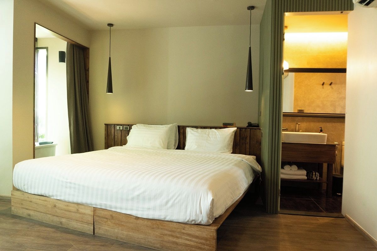 A bedroom with a wooden bed, a bedside table, a mirror, and a bathroom with a sink and towel rack.