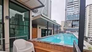 A rooftop swimming pool with wooden decking and white chairs, surrounded by high-rise buildings. - Tints of Blue Hotel (Bangkok)