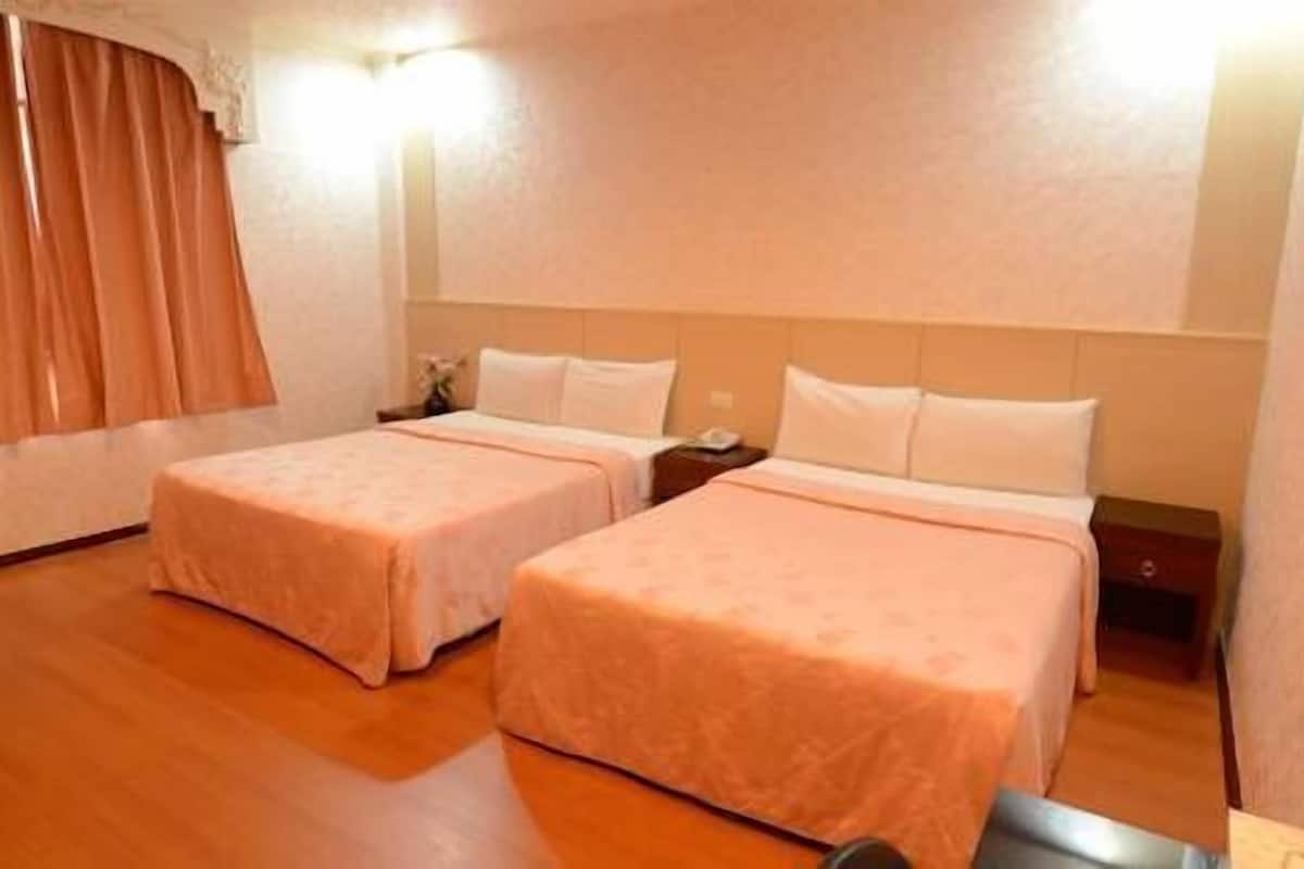 A hotel room with two beds, a nightstand, a lamp, and a window with curtains.