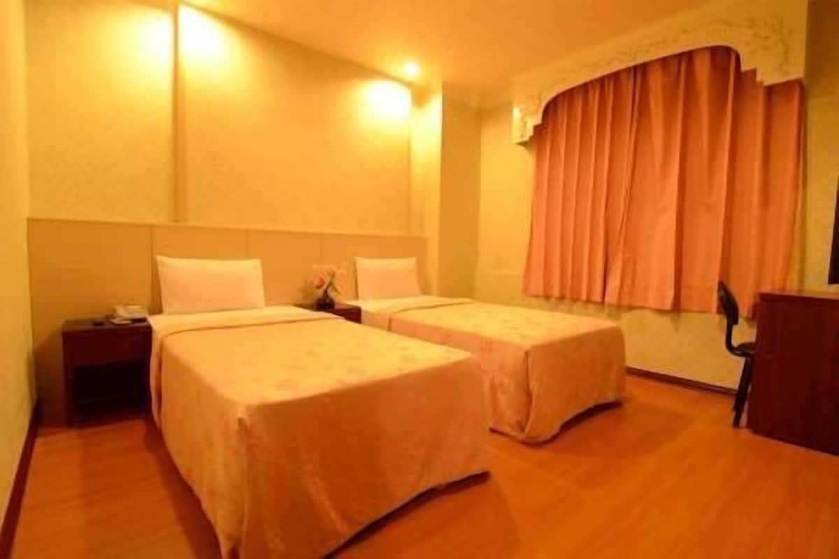 A hotel room with two single beds, a nightstand, a desk, and a window with curtains.