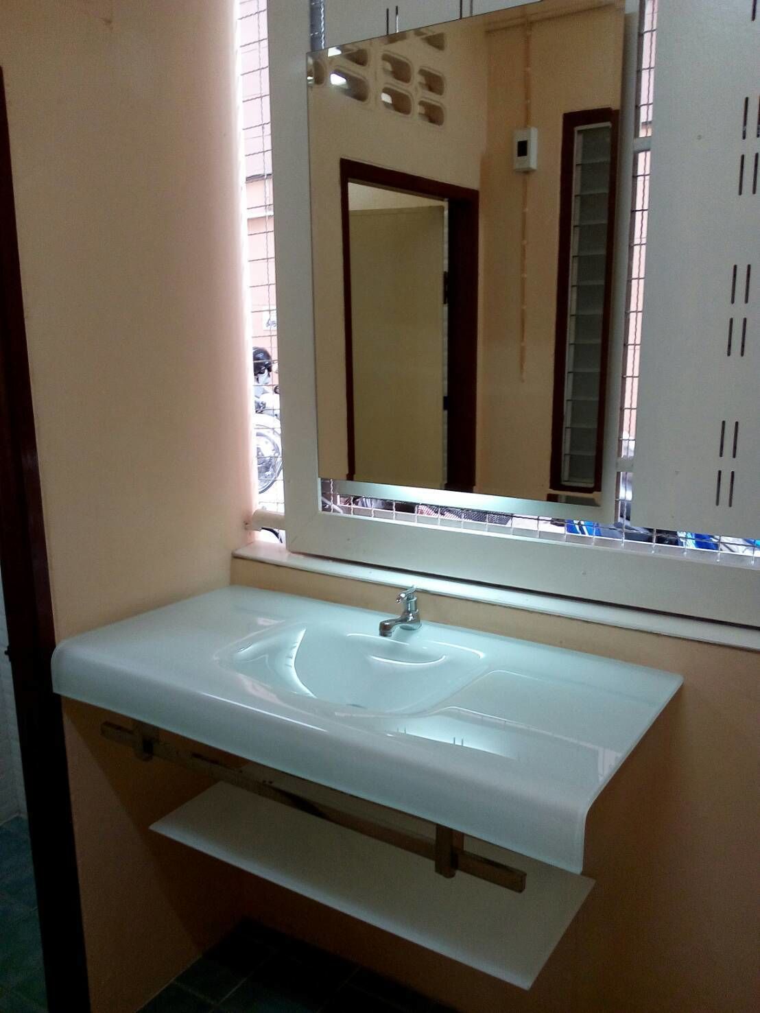 Un baño con lavamanos blanco, un espejo y una ventana con persianas.