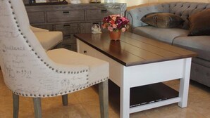 Una sala de estar con un sillón blanco, una mesa de centro de madera y un sofá gris.
