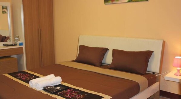 A neatly made bed with a brown bedspread and two pillows, a bedside table with a lamp, and a bathroom visible in the background. - Navavilla (Khlong Luang)
