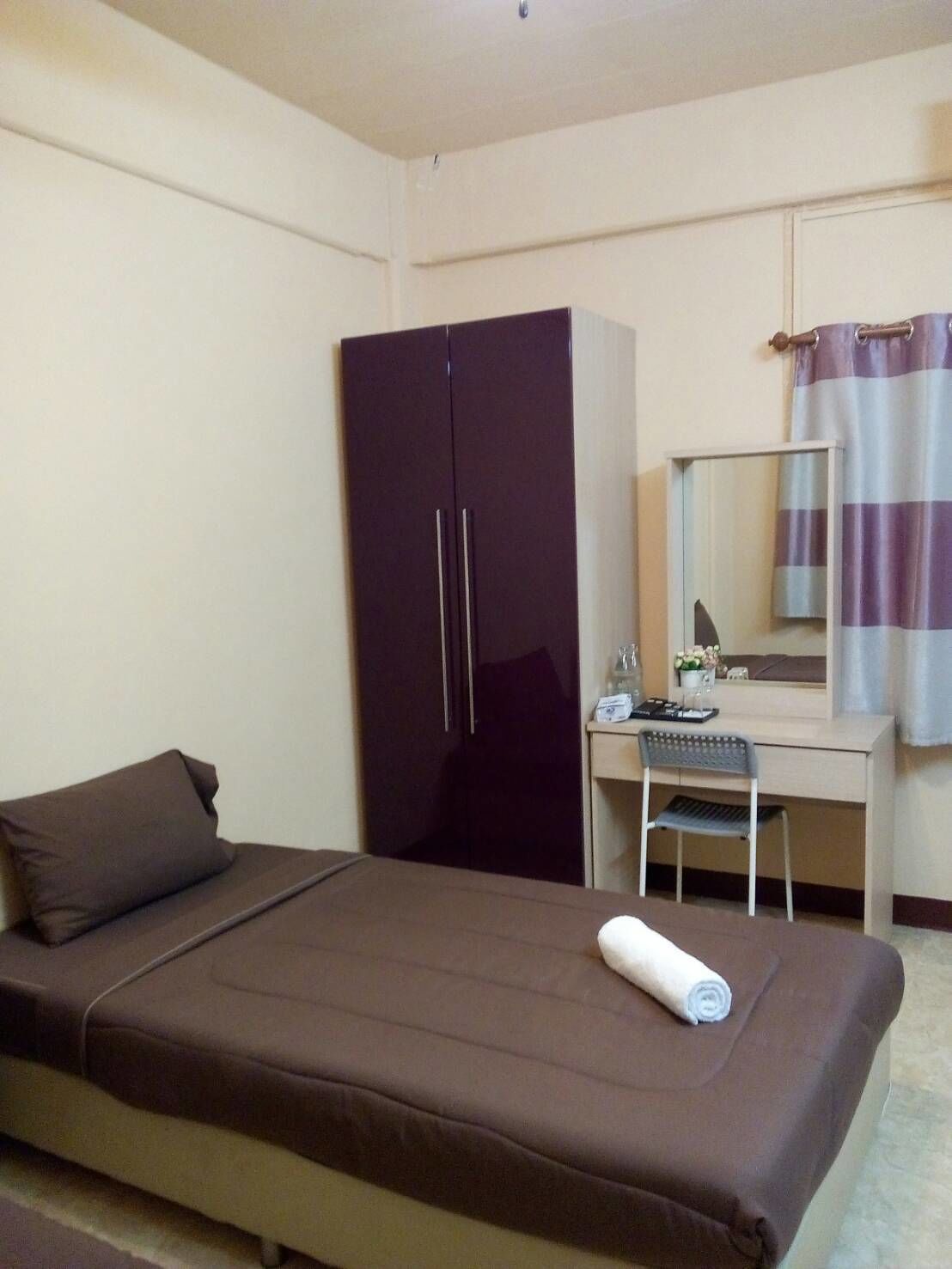 A bedroom with a single bed, a wardrobe, a desk with a chair, a mirror, and a bathroom with a striped curtain.